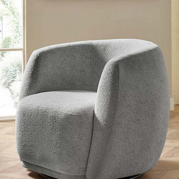 Grey textured barrel shaped awivel armchair in a room with a window and beige walls.