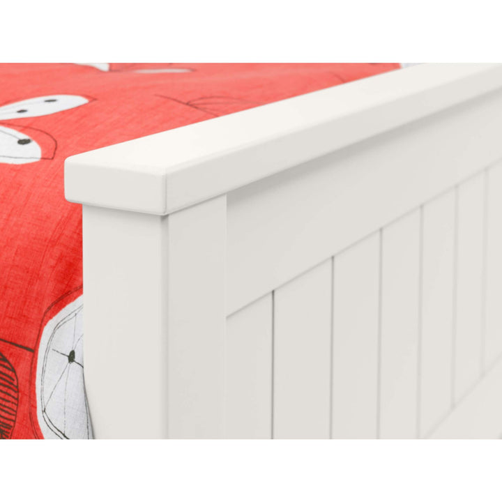 White bookcase bed close up with a red quilt on top.